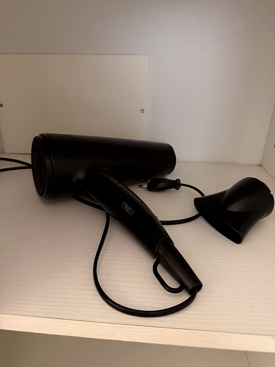 A black professional hairdryer with a separate concentrator nozzle, on a white shelf