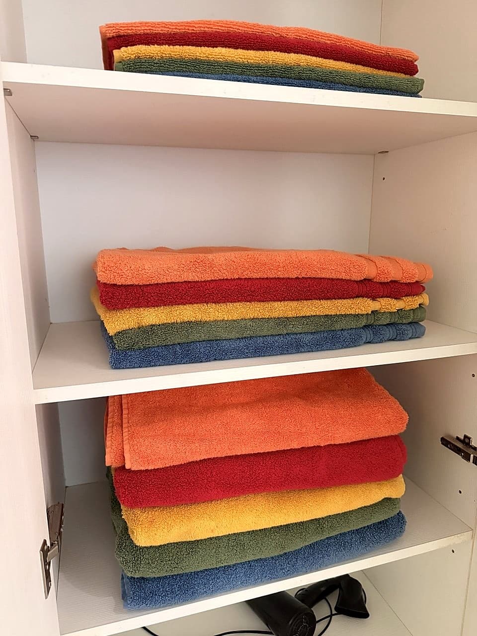 A second cupboard in the corridor just outside the bathroom, with additional stacks of colourful towels on three shelves