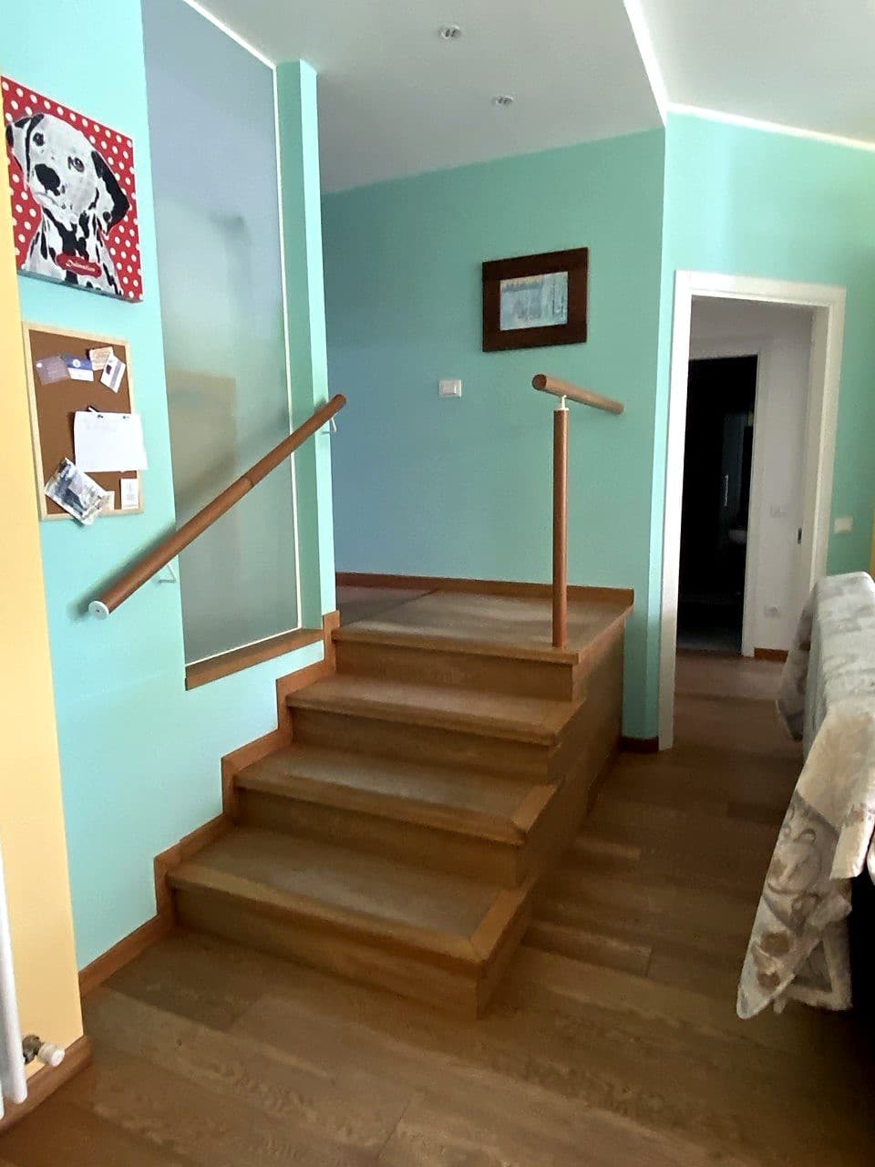 Die innere Holztreppe, die Eingang und Waschküche vom Hauptgeschoss der Wohnung trennt · ein Handlauf auf beiden Seiten (einer an der Wand, einer an einem Pfosten), blassgrüne Wände, links ein Pop-Gemälde eines getupften Dalmatiners mit roten Punkten
