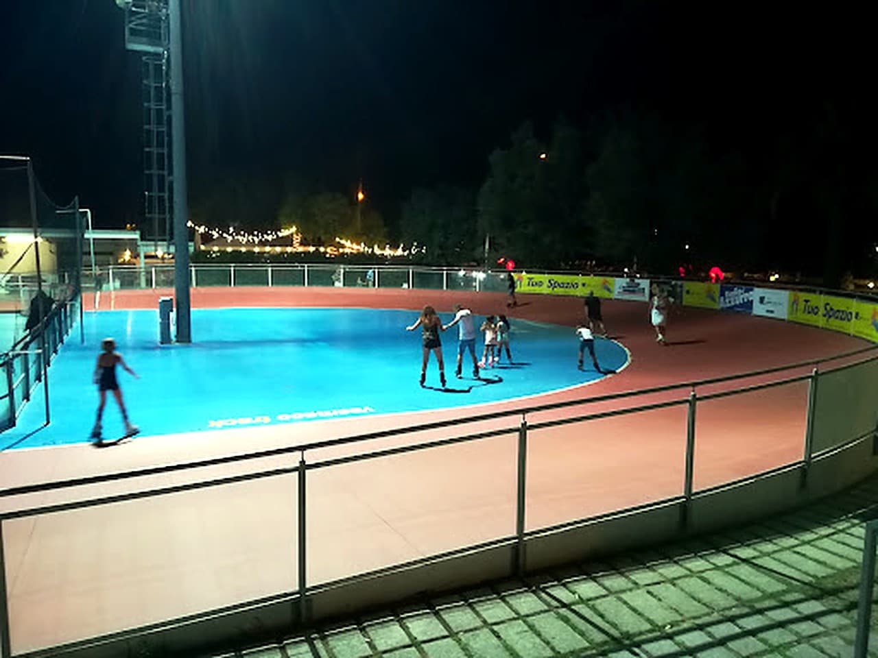Pista del Pattinodromo Panfili alla sera · allenamento sotto i riflettori, atleti sul piano, tribune e arena illuminate