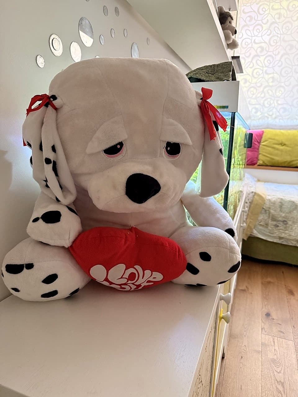 Grande peluche dalmatino con fiocchi rossi sulle orecchie, che tiene un cuore rosso con scritta LOVE